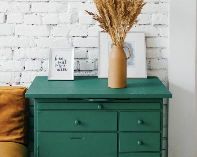 appealing photo of green wooden drawers against a white brick wall with a photo frame, vase and painting on top